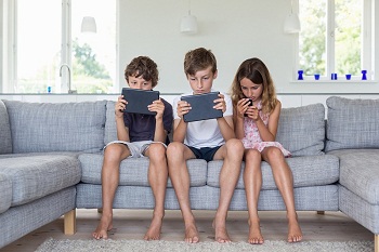 Brothers and sister on sofa with digital tablets and mobile